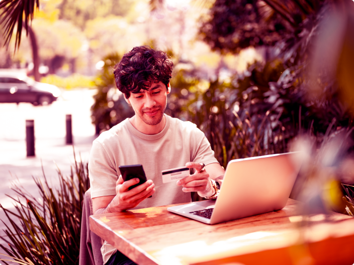 menino om o celular e o notebook verificando a segurança do site para fazer uma compra online