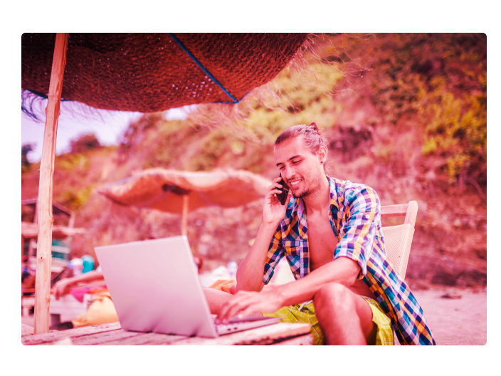 Homem que se tornou um nômade digital trabalhando na praia com seu notebook e conversando pelo seu celular
